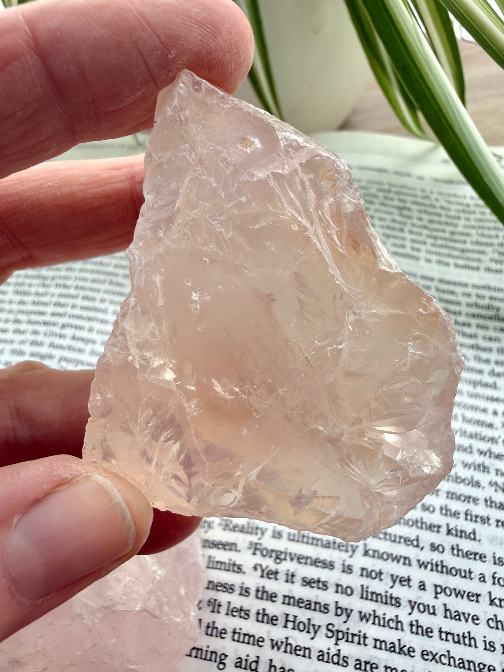 Rose quarrtz held between 2 fingers over a book 