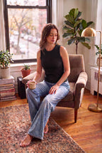 A hip-length bamboo crew neck tank featuring subtle textured detailing on a woman sitting in living room wearing jeans  - black coloured top 