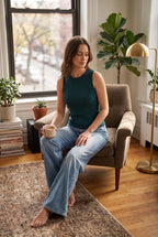 A hip-length bamboo crew neck tank featuring subtle textured detailing on a woman sitting in living room wearing jeans - emerald coloured top 