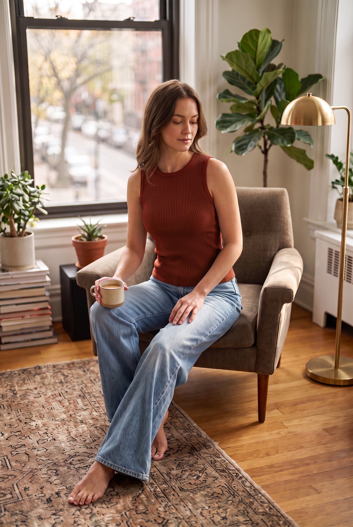 A hip-length bamboo crew neck tank featuring subtle textured detailing on a woman sitting in living room wearing jeans cayenne or cinnamon coloured top