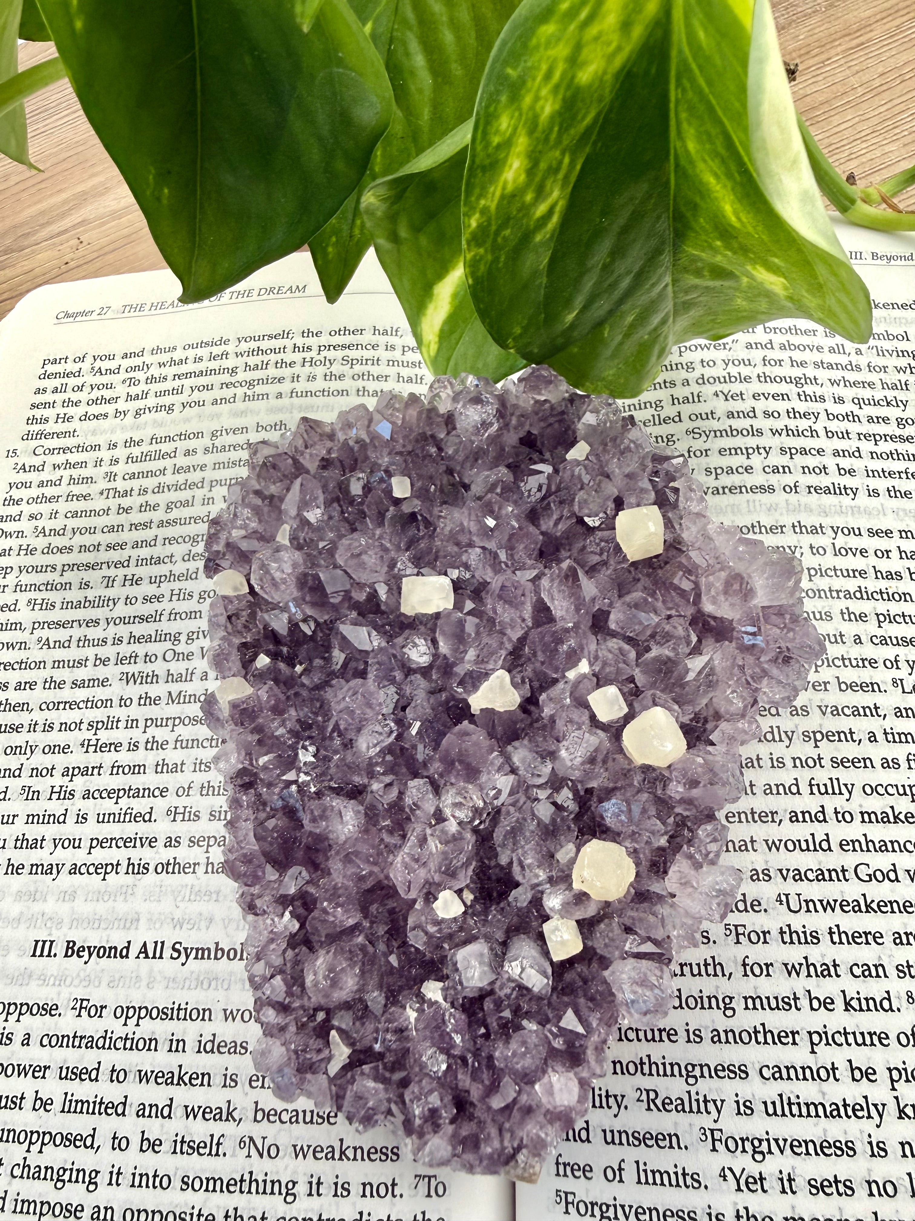 Amethyst cluster with calcite points lying flat on a book 
