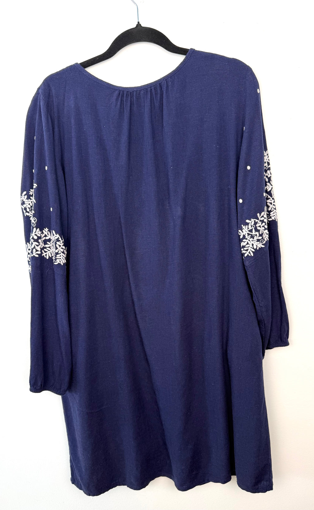Back view showing relaxed silhouette of navy dress with white embroidery on white wall