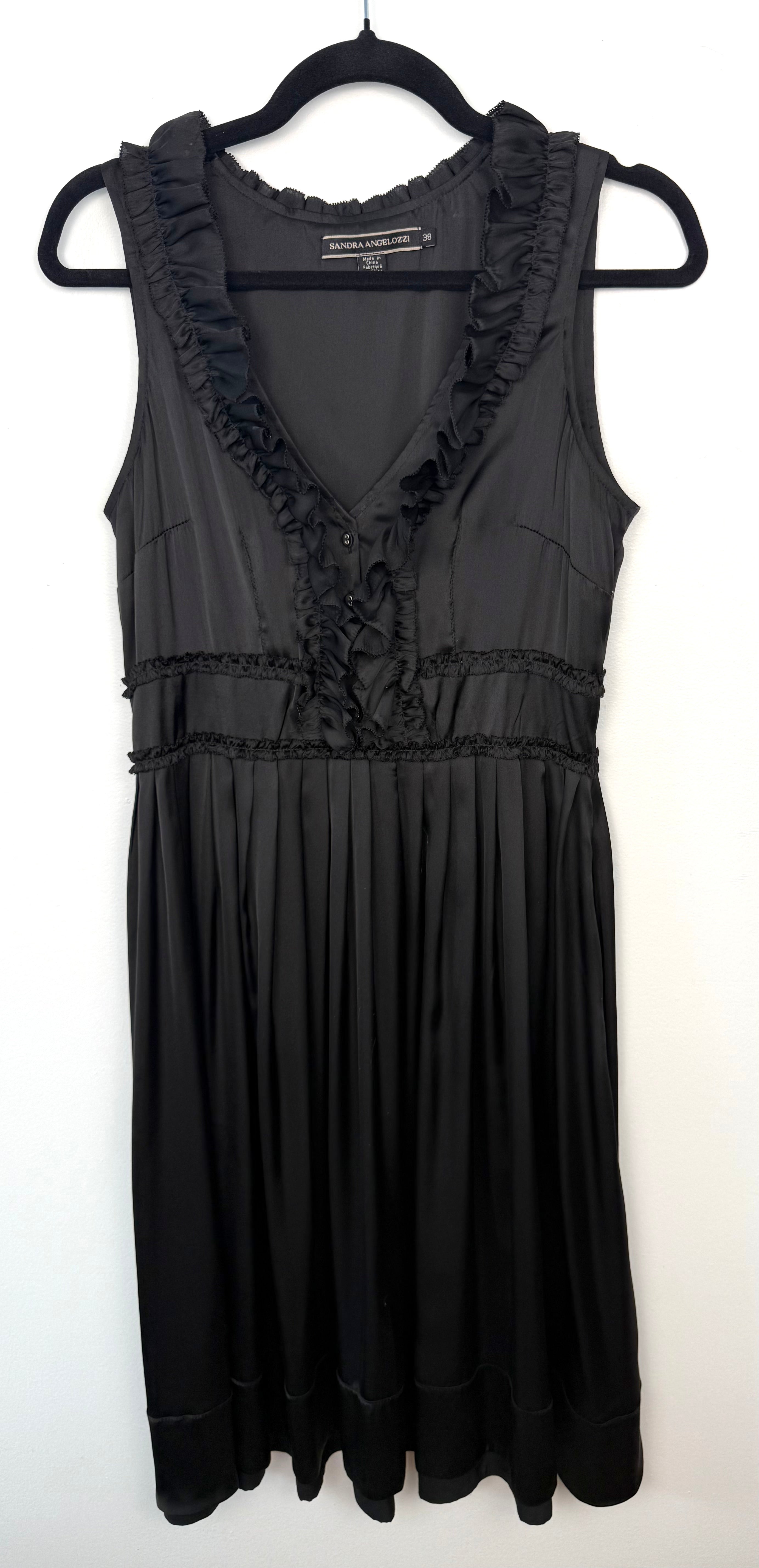 Black Sandra Angelozzi sleeveless dress with ruffle trim V-neckline and gathered waist, hanging on black hanger against white wall.