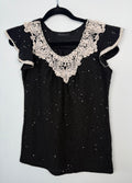 Black sequin knit top with cream crochet lace neckline hanging on black hanger