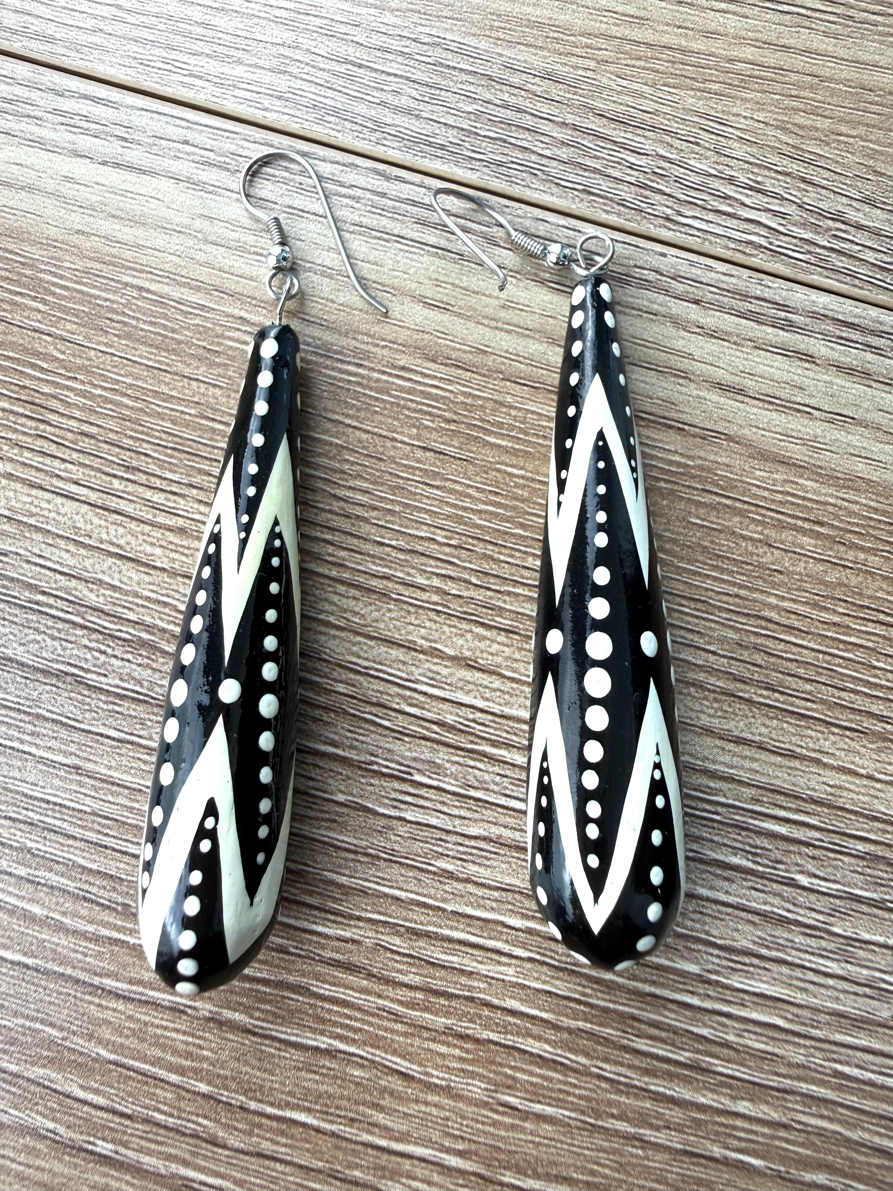 Black and white geometric long teardrop drop earrings with dotted tribal pattern on wood background.