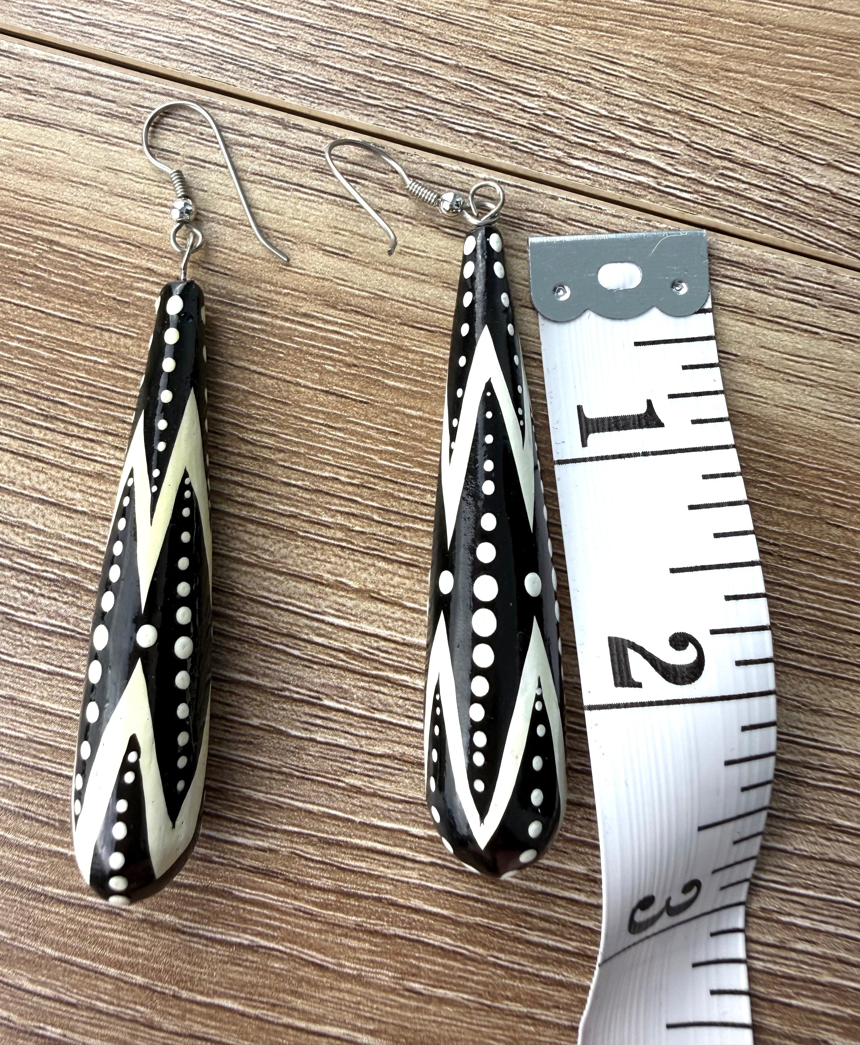 Close-up of black and white patterned statement dangle earrings beside measuring tape showing length.