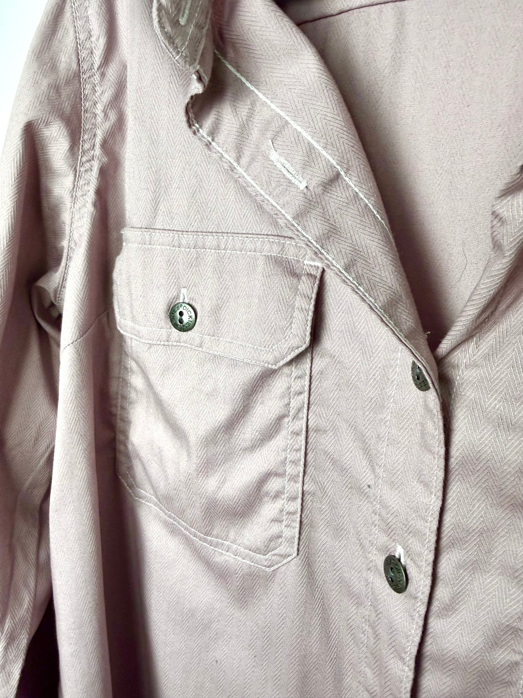 Close up of Dickies branded button and cargo flap chest pocket on dusty rose coloured herringbone work shirt.