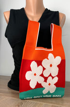 Colourful knit tote bag with white flowers and “You Only Live Once” text shown on mannequin for scale