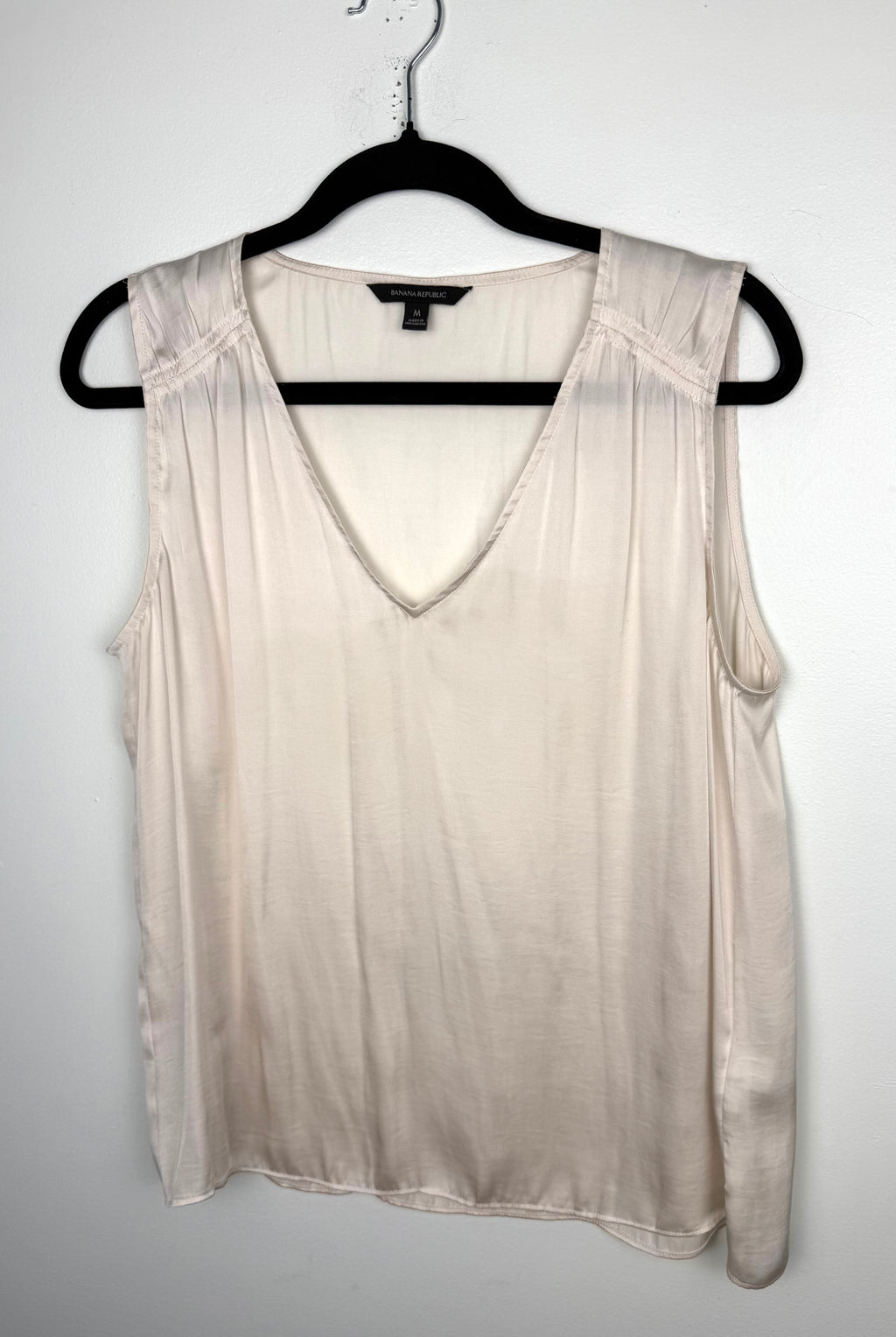 front of Cream Banana Republic sleeveless blouse featuring a V-neckline, gathered shoulder detail, relaxed silhouette, and fluid drape throughout the body. on hanger