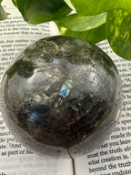Labradorite crystal ball on an open book with green leaves in the background