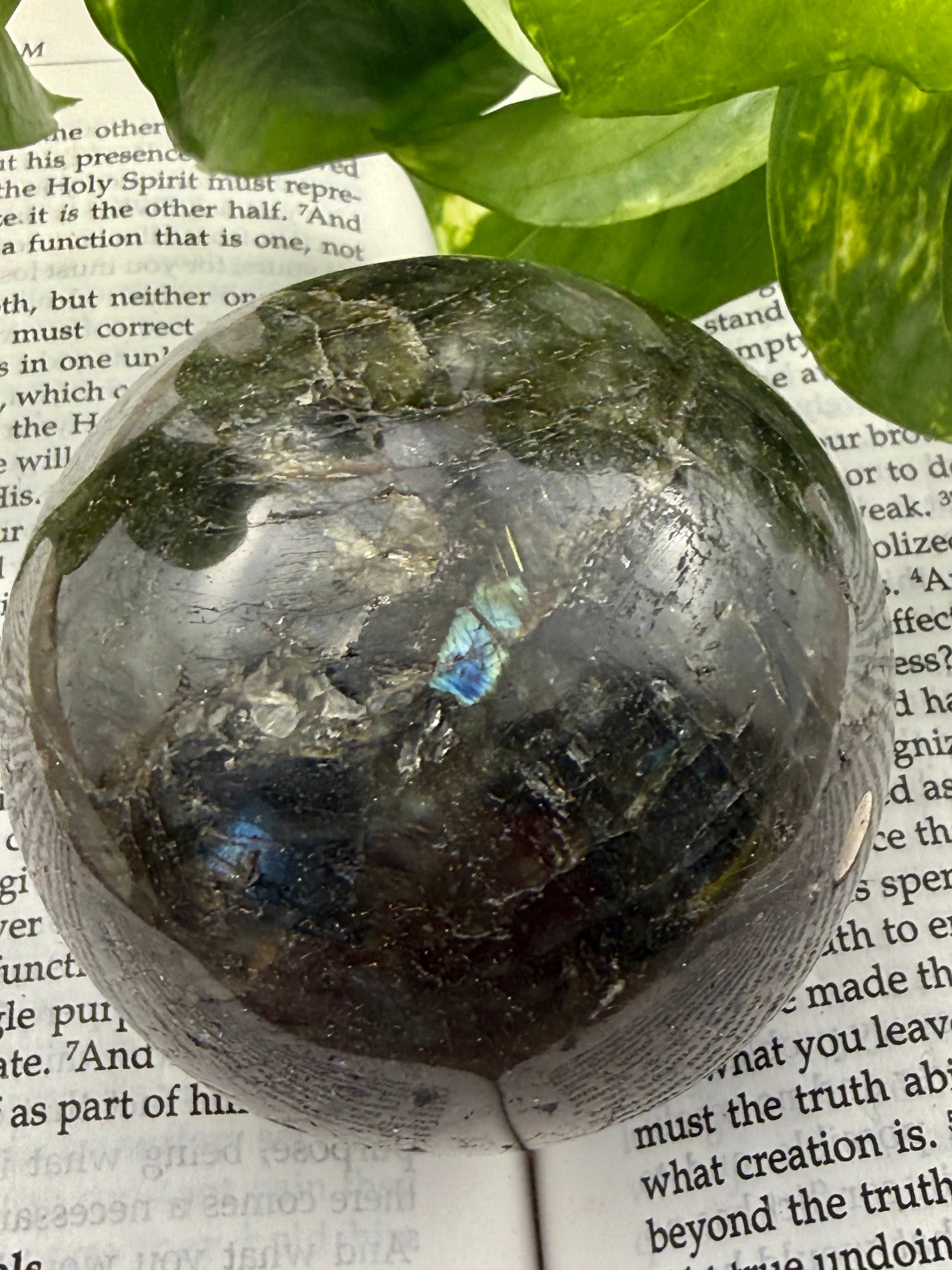Labradorite crystal ball on an open book with green leaves in the background