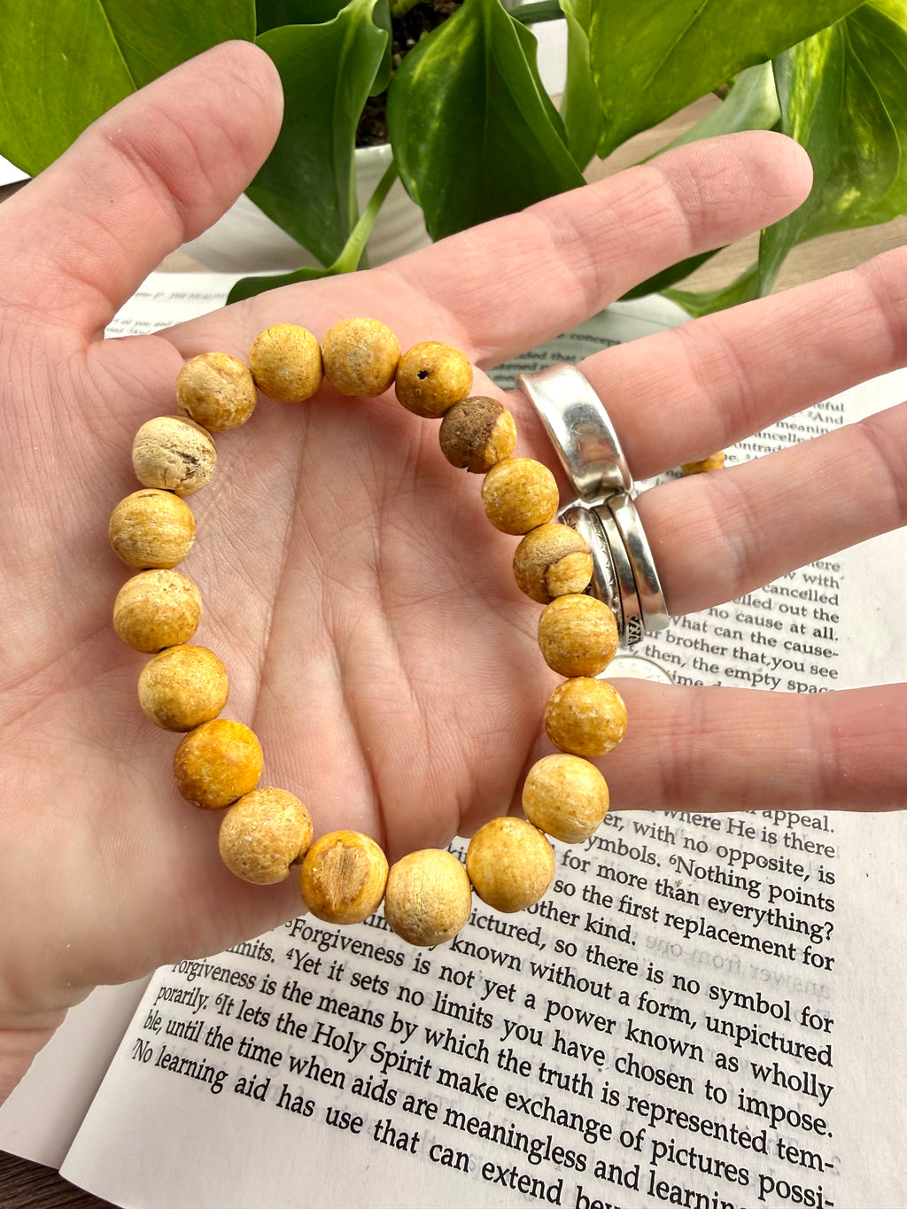 Hand wearing a yellow beaded bracelet on an open book with green leaves in the background