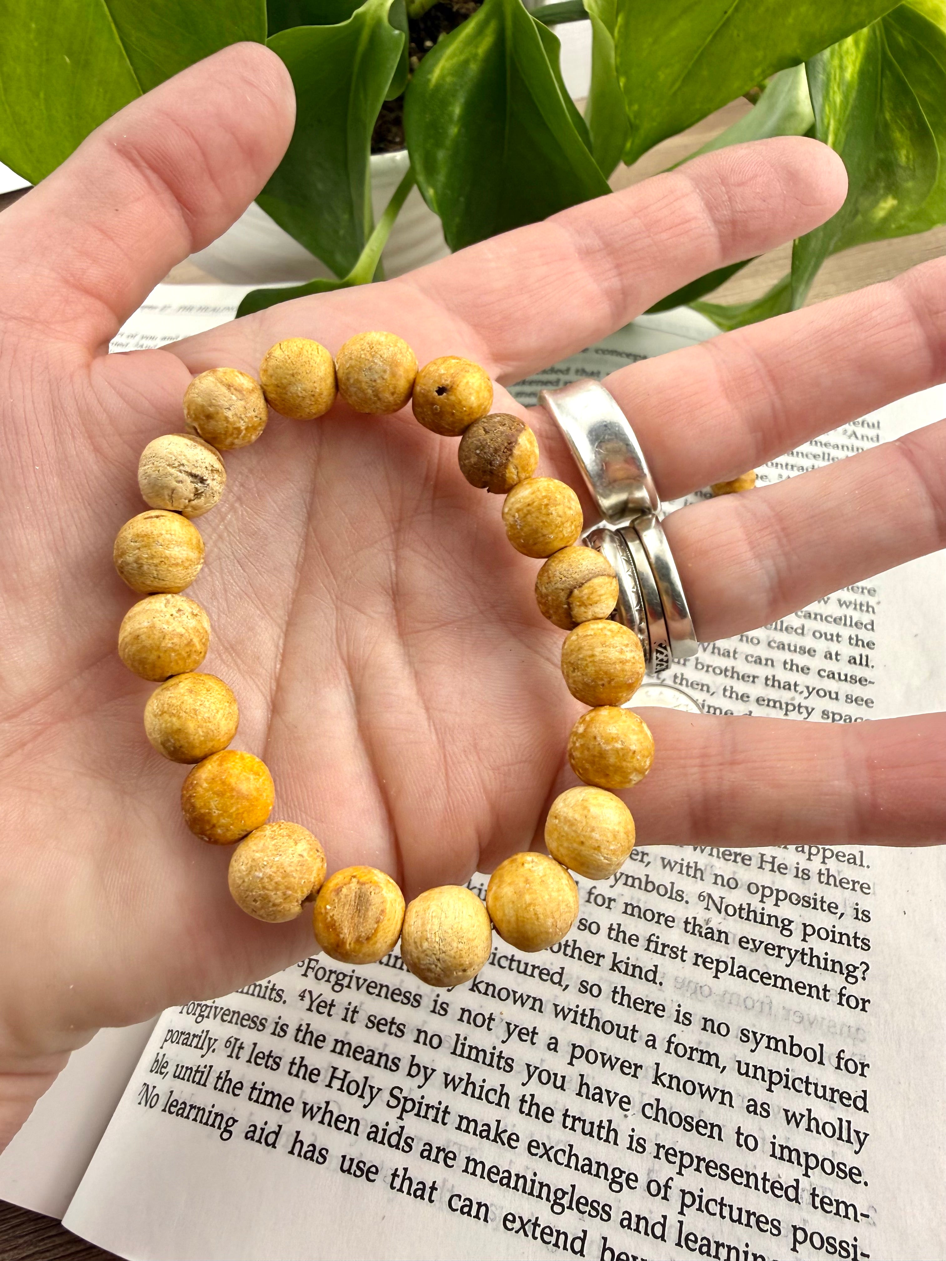 Hand wearing a yellow beaded bracelet on an open book with green leaves in the background