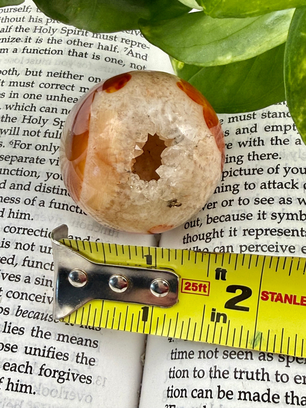 Decorative stone with a central hole on top of a book, with a measuring tape for scale.