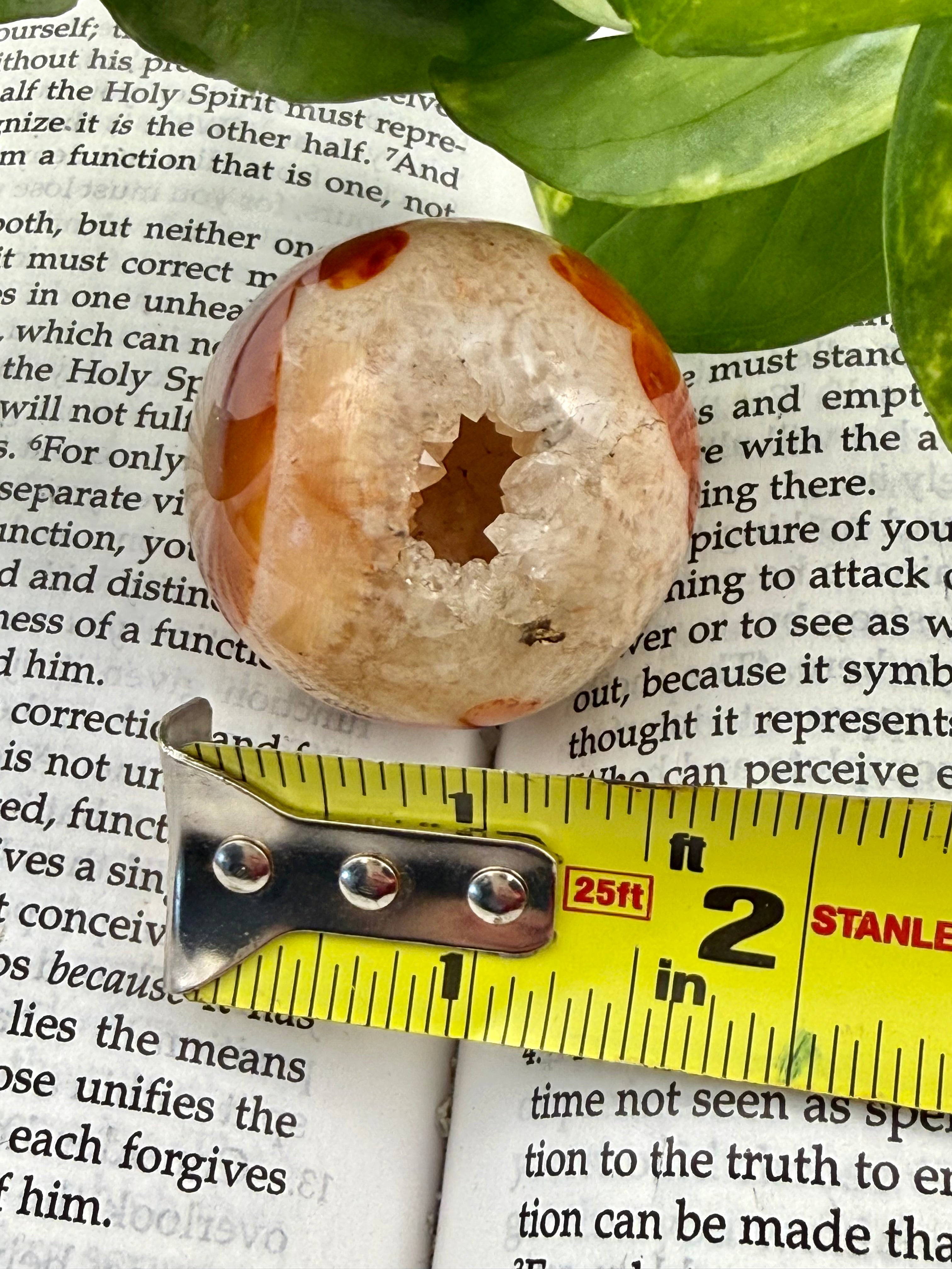 Decorative stone with a central hole on top of a book, with a measuring tape for scale.