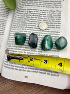 Four green malachite stones on an open book with a ruler for scale.