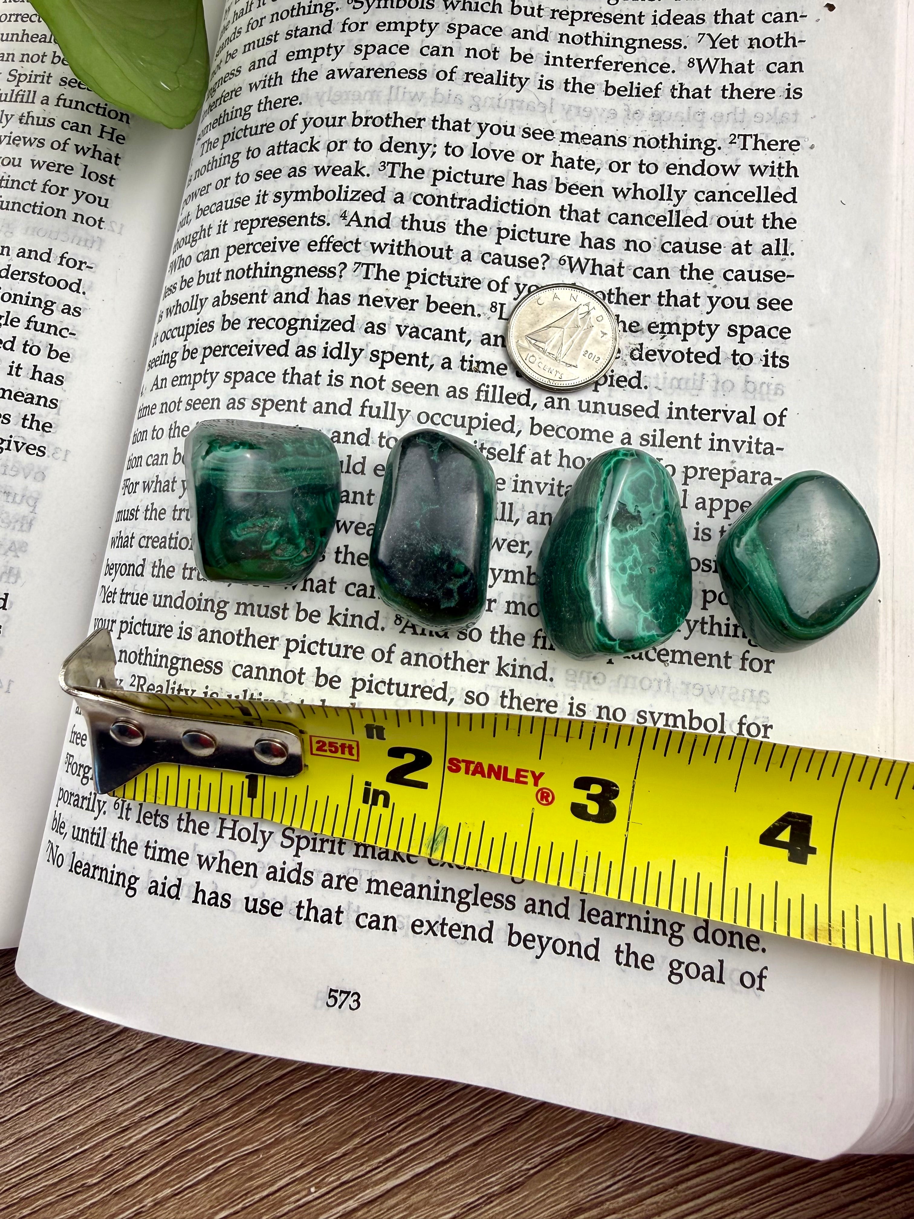 Four green malachite stones on an open book with a ruler for scale.