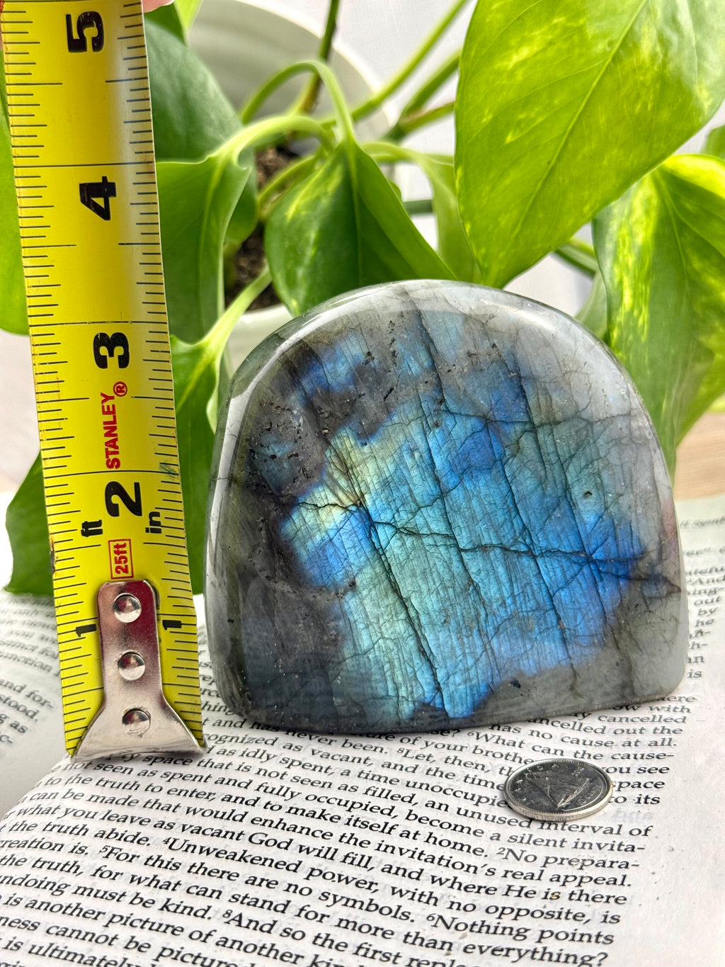 Labradorite stone with blue and green patterns on a piece of paper, next to a measuring tape.