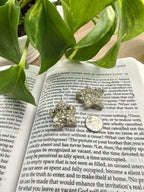 Open book with a decorative stone on top, surrounded by green leaves. stones are pyrite stars