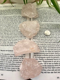 4 rose quartz crystals on top of a book with green leaves in the background