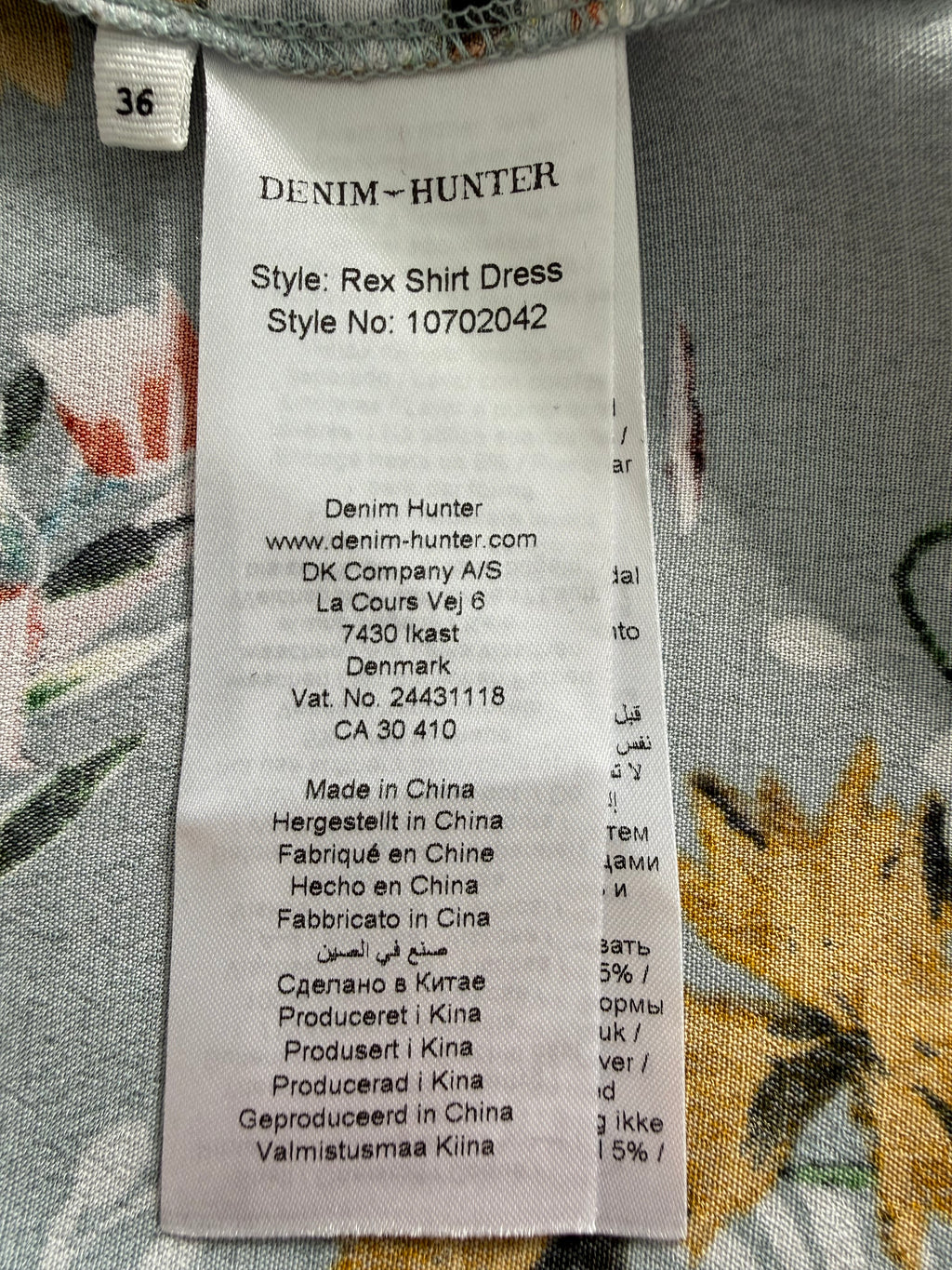 Clothing label on a floral fabric background -Denim Hunter Rex shirt dress EU 36 label