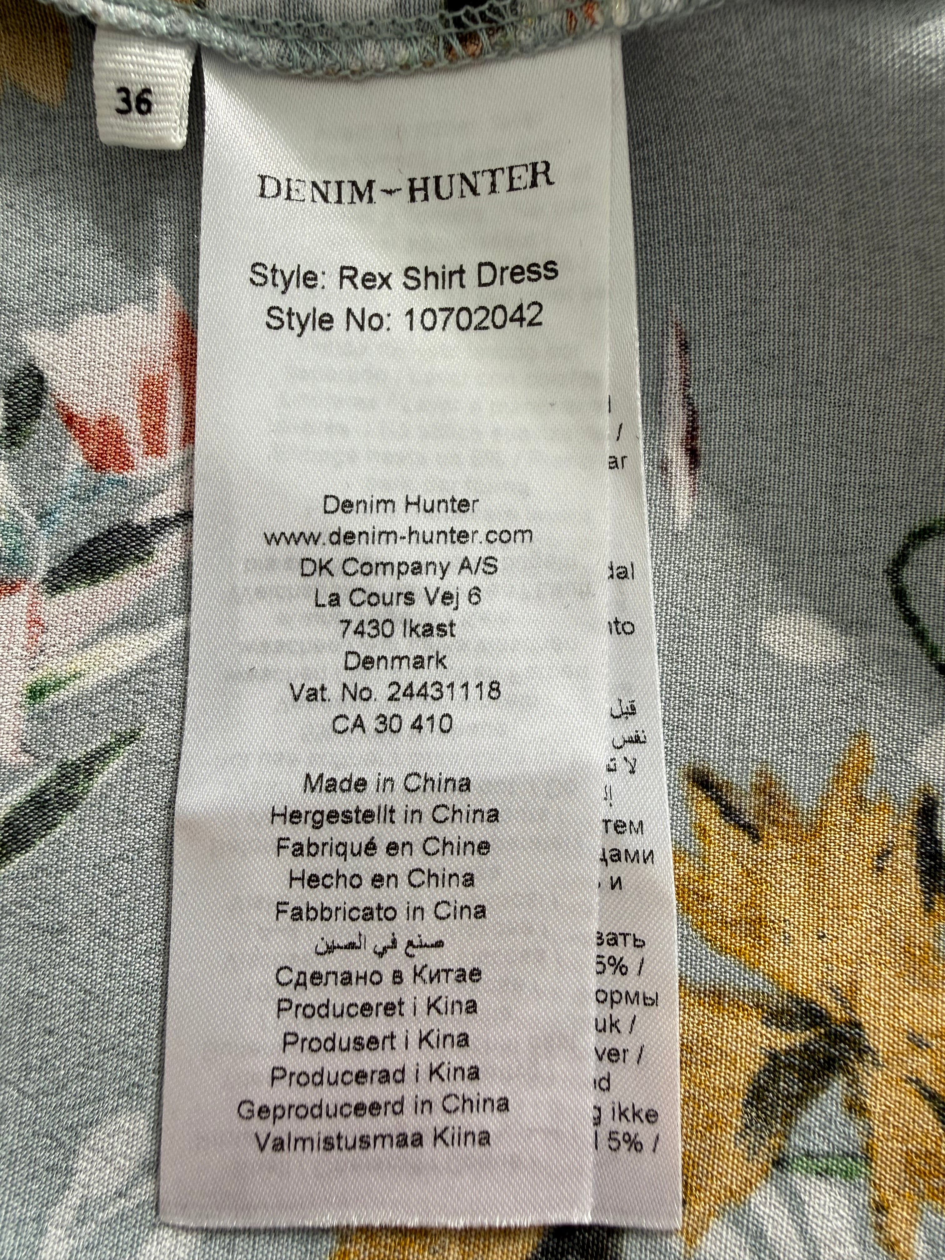 Clothing label on a floral fabric background -Denim Hunter Rex shirt dress EU 36 label