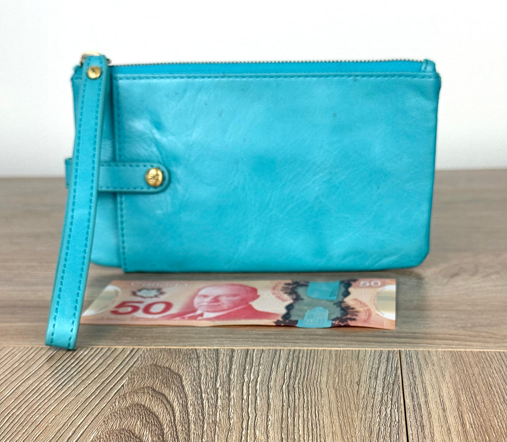 Turquoise HOBO Evolve leather wristlet clutch with gold hardware and detachable strap shown next to Canadian $50 bill for size reference.