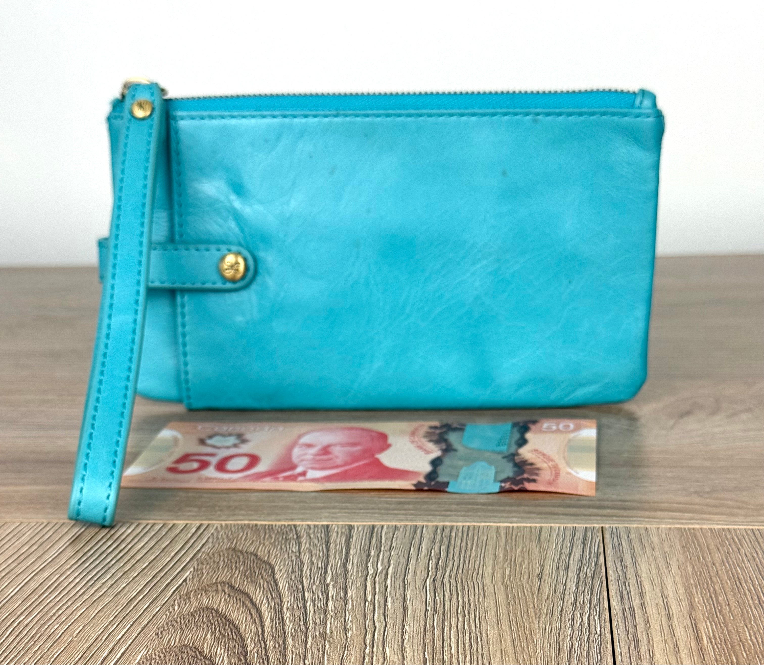 Turquoise HOBO Evolve leather wristlet clutch with gold hardware and detachable strap shown next to Canadian $50 bill for size reference.
