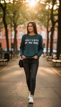 H&M Divided teal green 100% cotton graphic crew neck sweatshirt with "Property of No One" distressed white lettering, front view on hanger — Blue Sparrow pre-loved women's fashion on woman walking outside