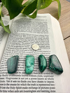 Four green  malachite stones on an open book with a plant in the background