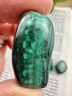 Green malachite stone held between fingers with a blurred background