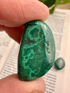 Greenish-blue stone held between fingers on a paper background