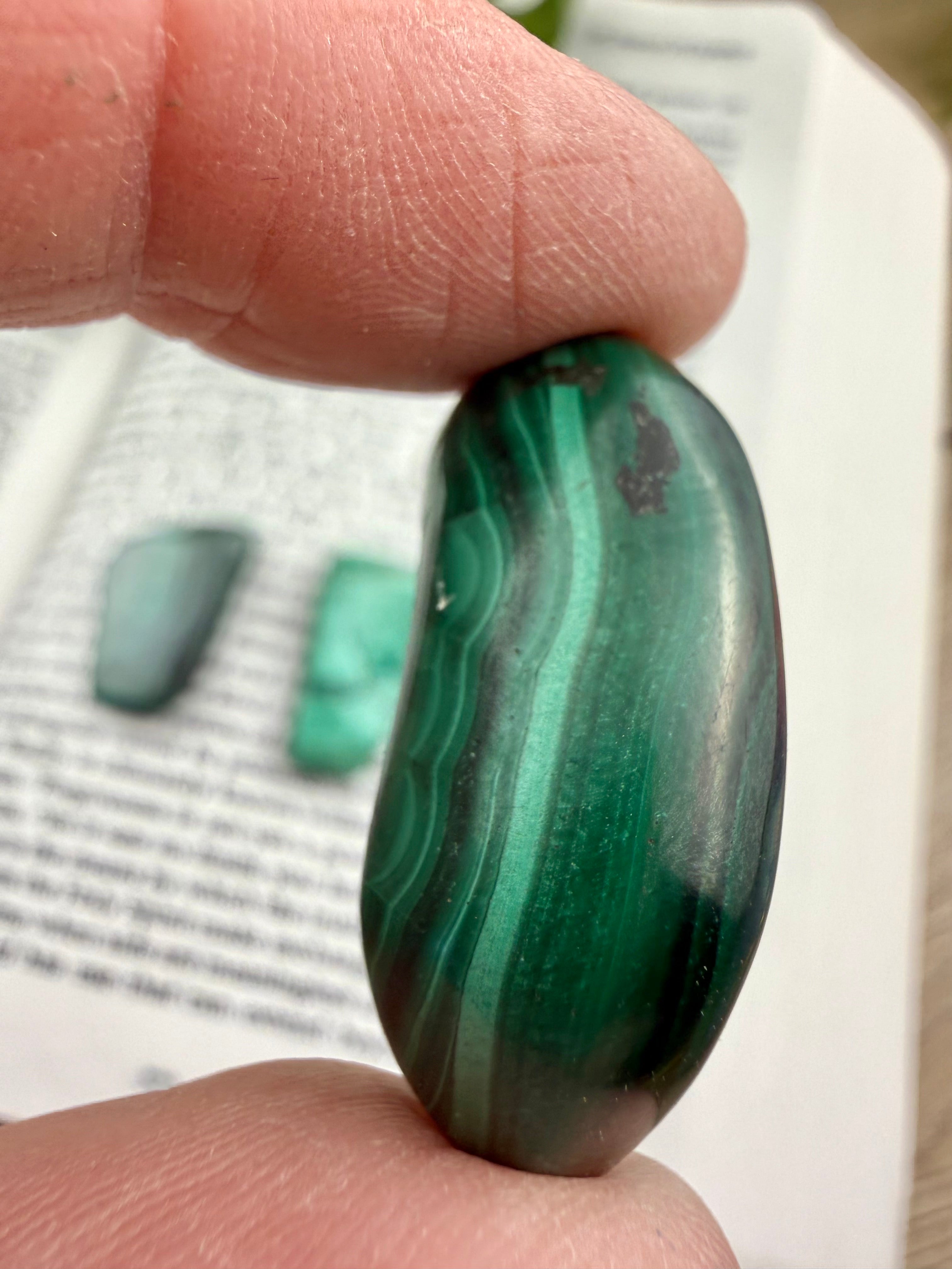 Malachite stone held between fingers with a blurred background