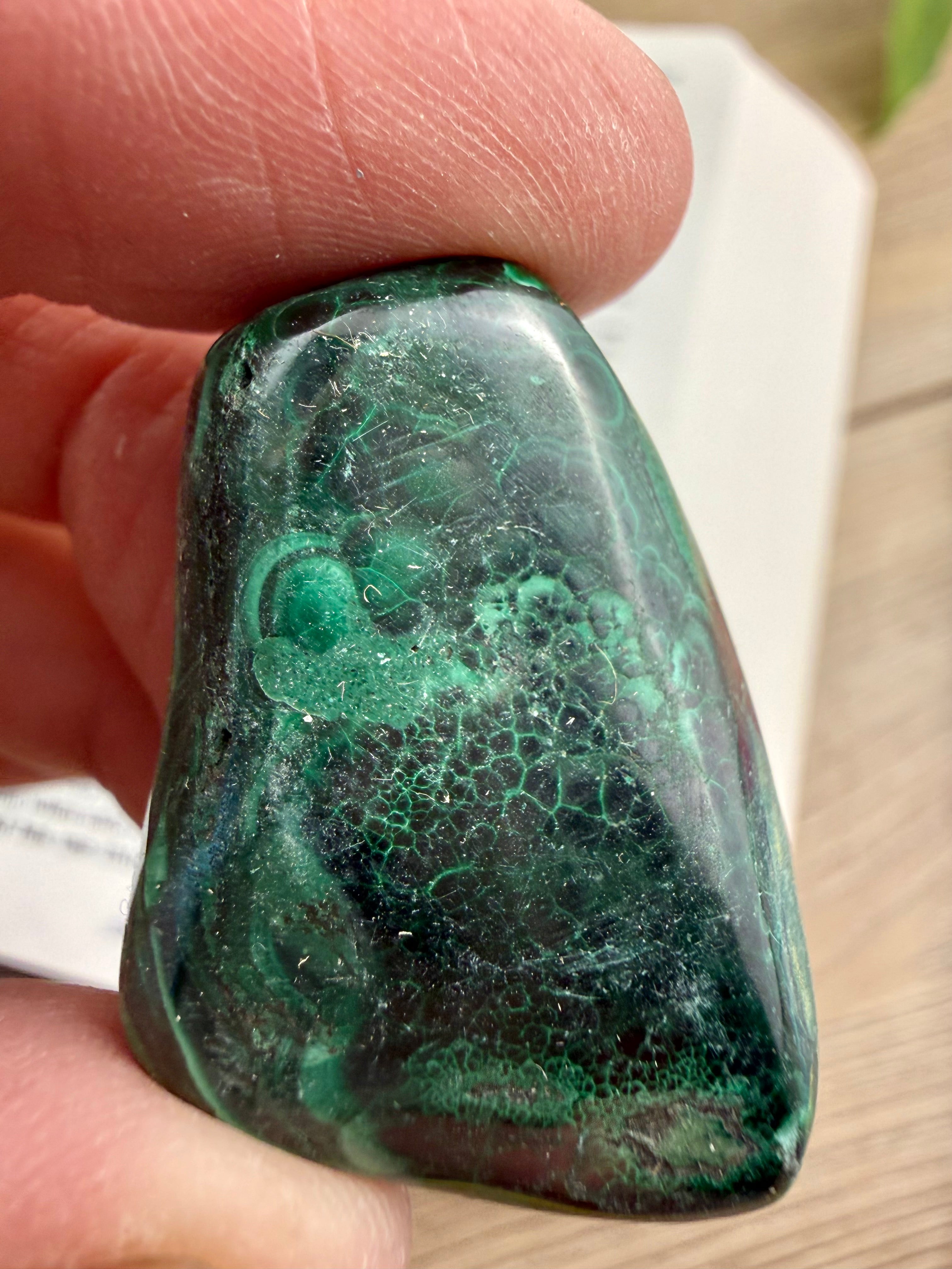 Green and black marbled stone held between fingers on a wooden surface