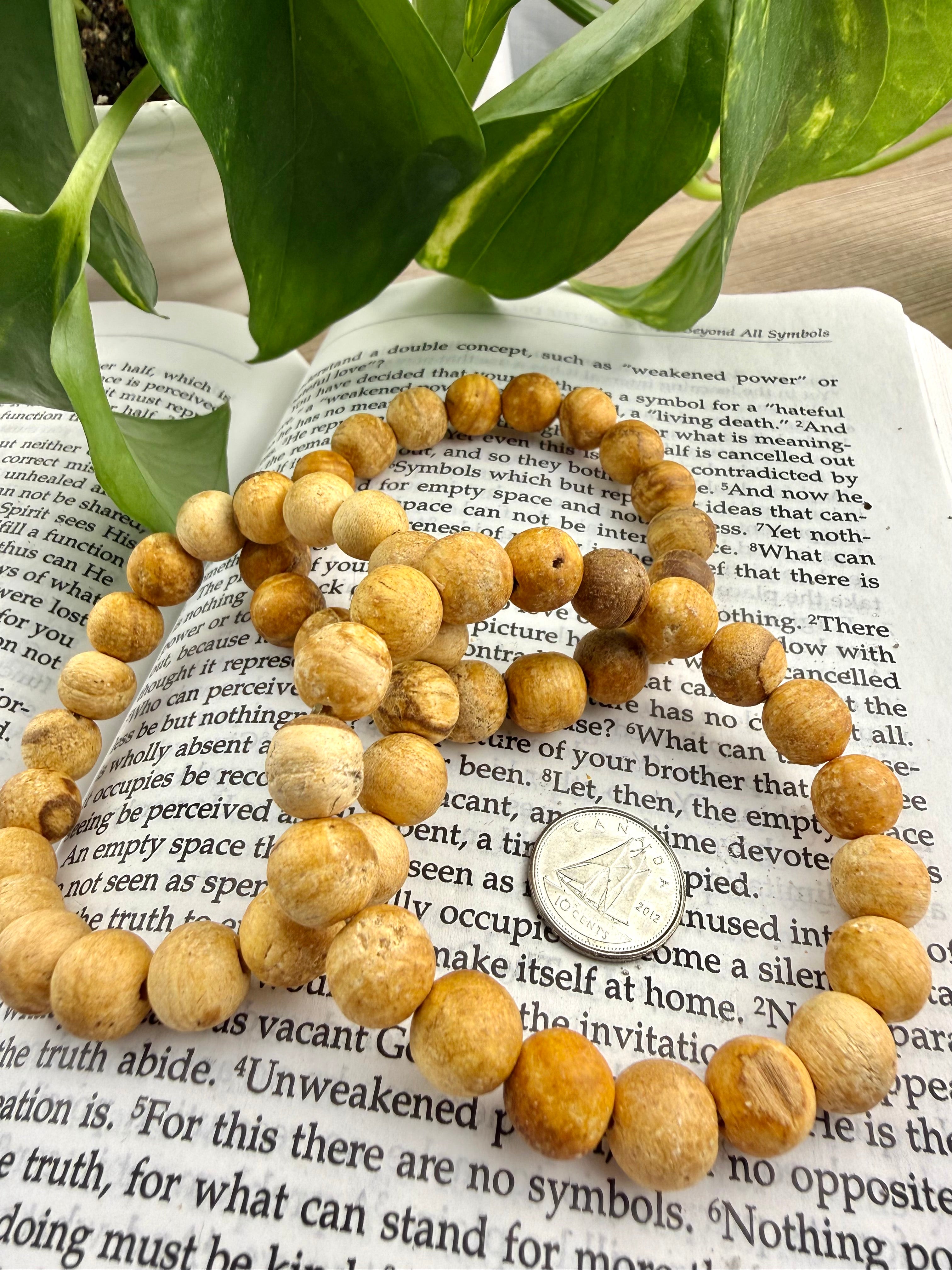 3 wooden beaded bracelet son an open book with green leaves in the background