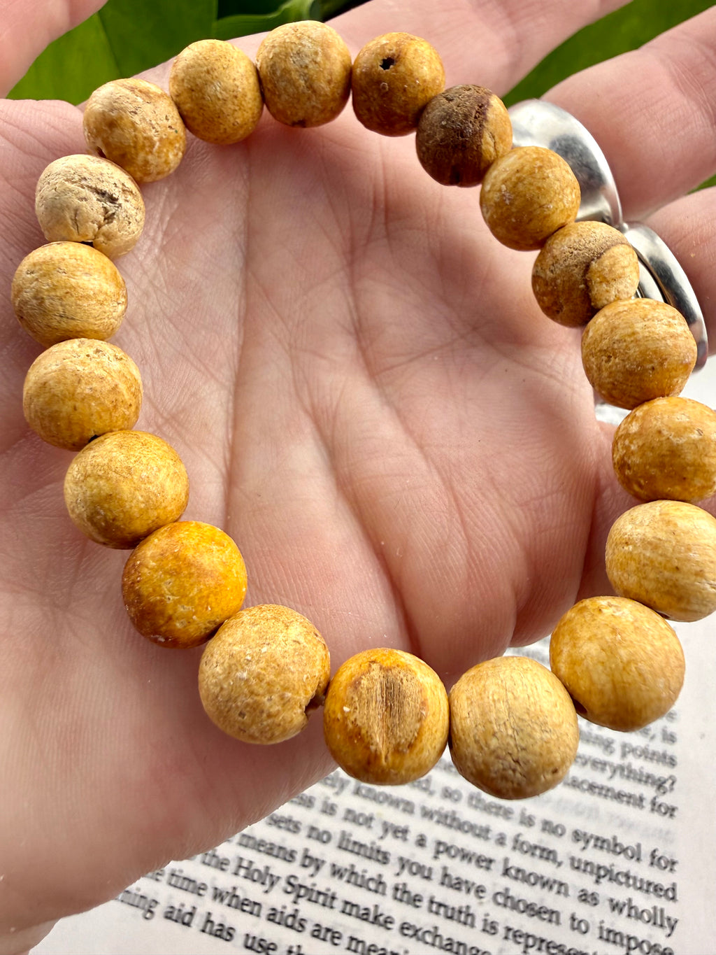 Hand wearing a bracelet with yellow-beige beads on a book page background