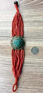 Red artisan beaded bracelet with turquoise medallion shown with coin for scale