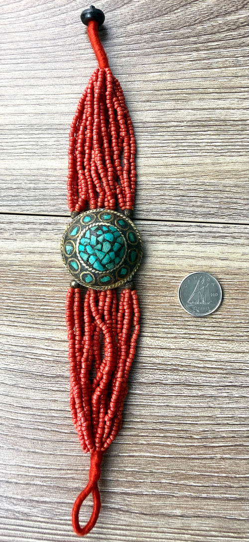 Red artisan beaded bracelet with turquoise medallion shown with coin for scale