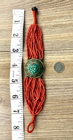 Red adjustable seed bead bracelet approximately 8 inches long with turquoise centre