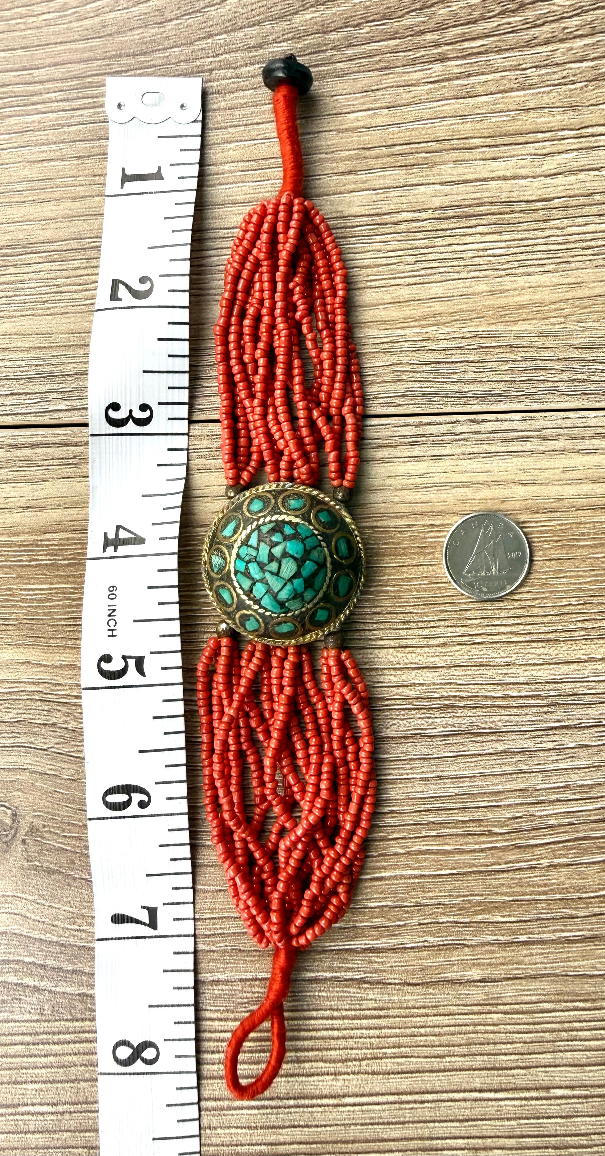 Red adjustable seed bead bracelet approximately 8 inches long with turquoise centre