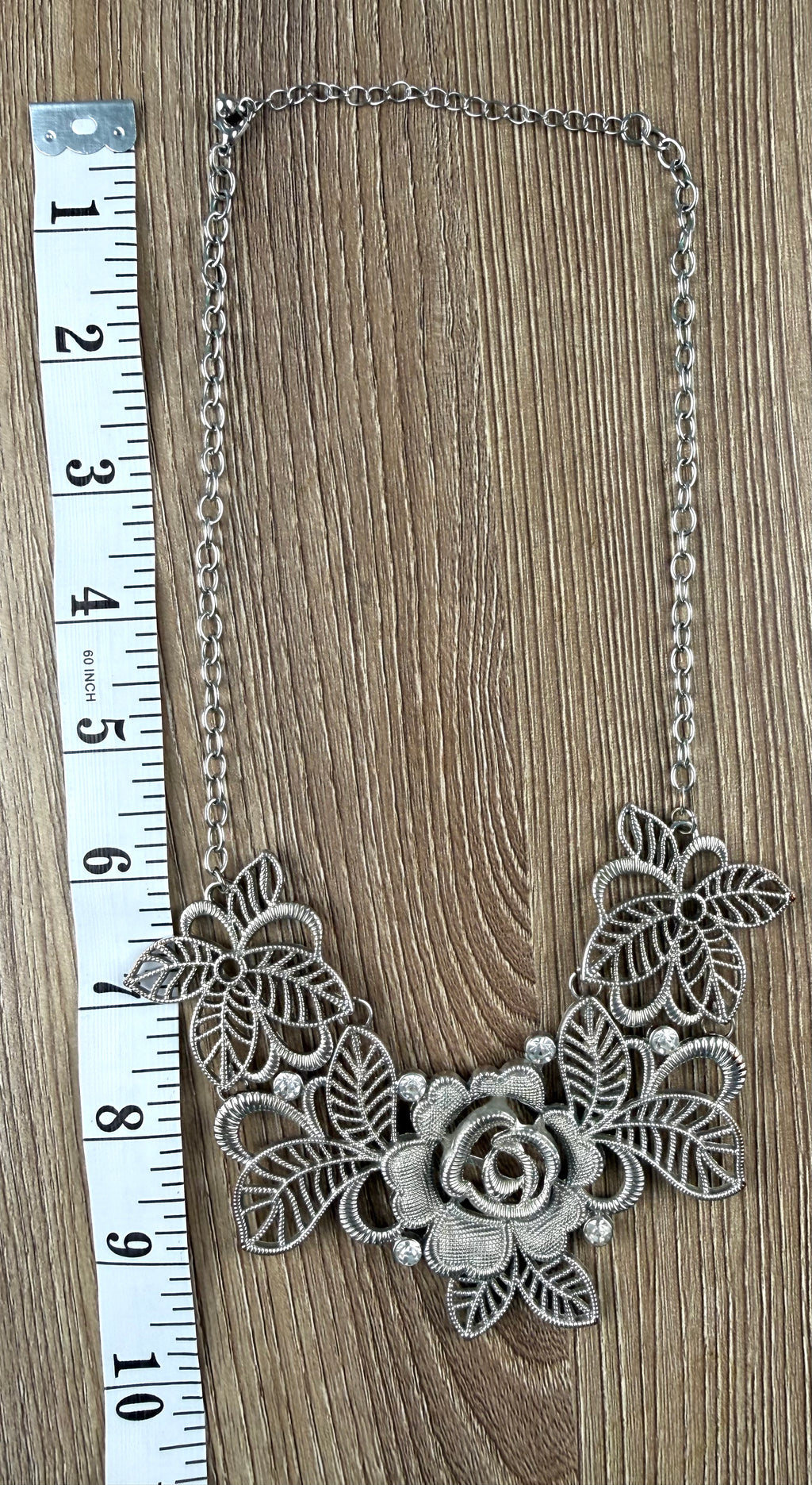 Silver-tone filigree rose bib necklace laid flat with measuring tape, full length view, openwork floral and leaf pendant, crystal accents — Blue Sparrow pre-loved jewellery