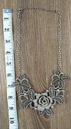 Silver-tone filigree rose bib necklace laid flat with measuring tape, full length view, openwork floral and leaf pendant, crystal accents — Blue Sparrow pre-loved jewellery