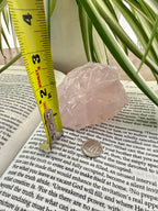 Rose quartz on  a book with a tape measure next to it, surrounded by green leaves