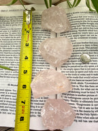 4 Rose Quartz crystals on a book with a measuring tape for scale